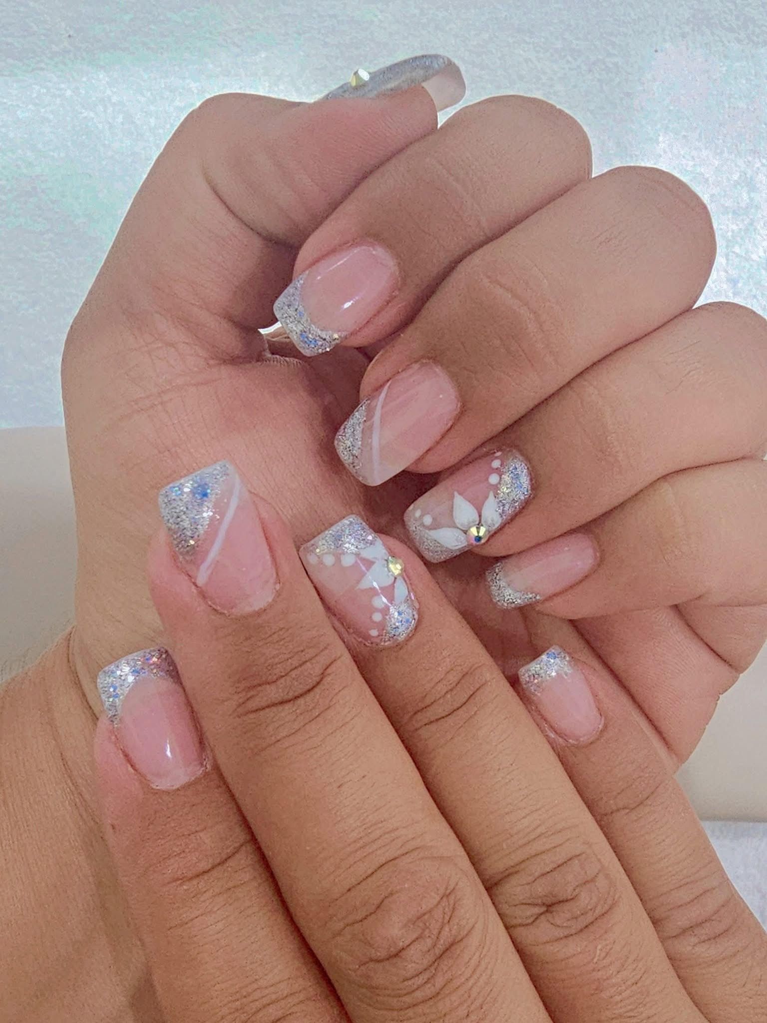 Close-up of hands with light pink nails, white and silver glitter accents, and floral designs.