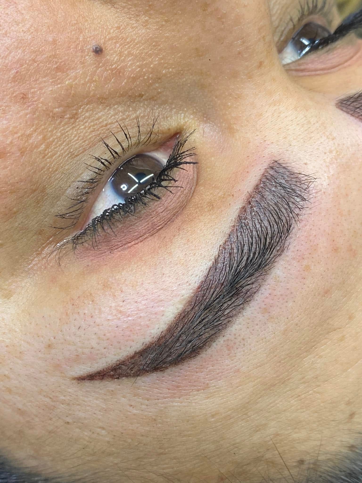 Close-up of a face with dark, curved eyebrow tattoo and eye with mascara.