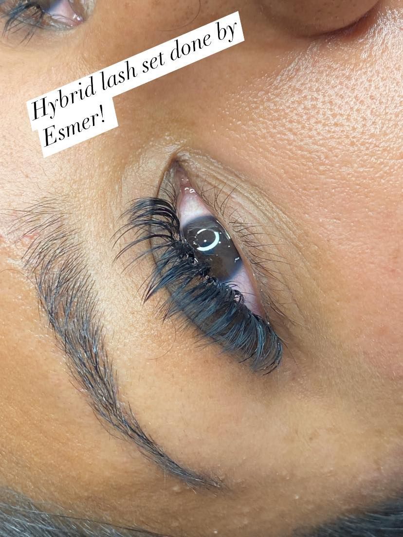 Close-up of an eye with a hybrid lash set. Dark lashes are attached, above a dark eyebrow.