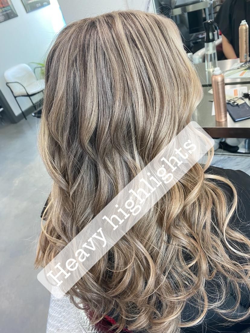 Woman with wavy, blonde hair, styled with heavy highlights, in a salon setting.