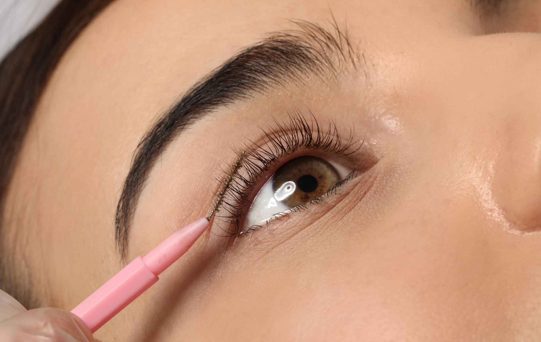 Person getting eyeliner tattoo applied near the eye; pink pencil in use.
