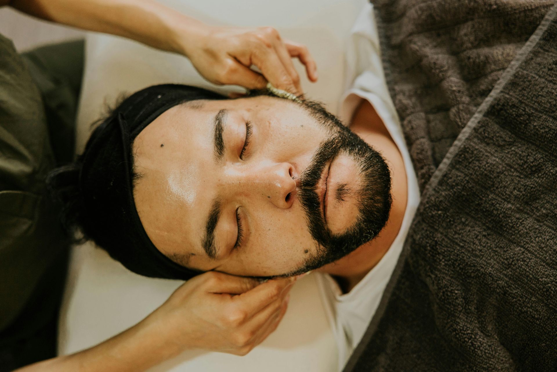 Person receiving a facial massage with eyes closed, lying on a treatment bed under a blanket