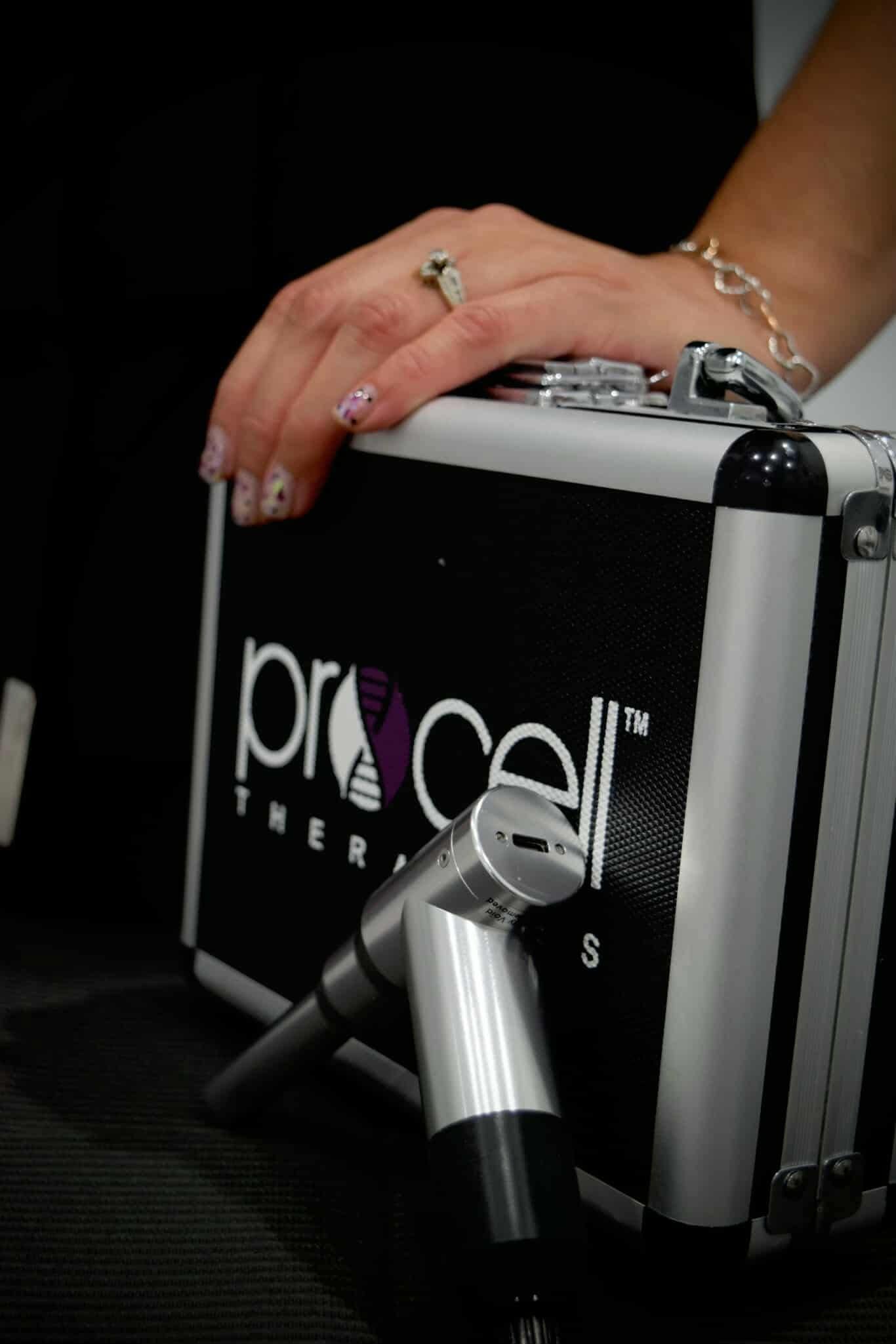 Person's hand with ring on ProCell Therapy device case, silver applicator nearby.