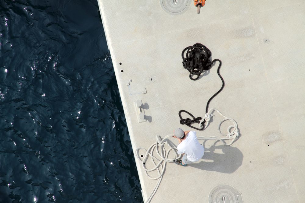 Person on a dock handling ropes beside dark blue water.