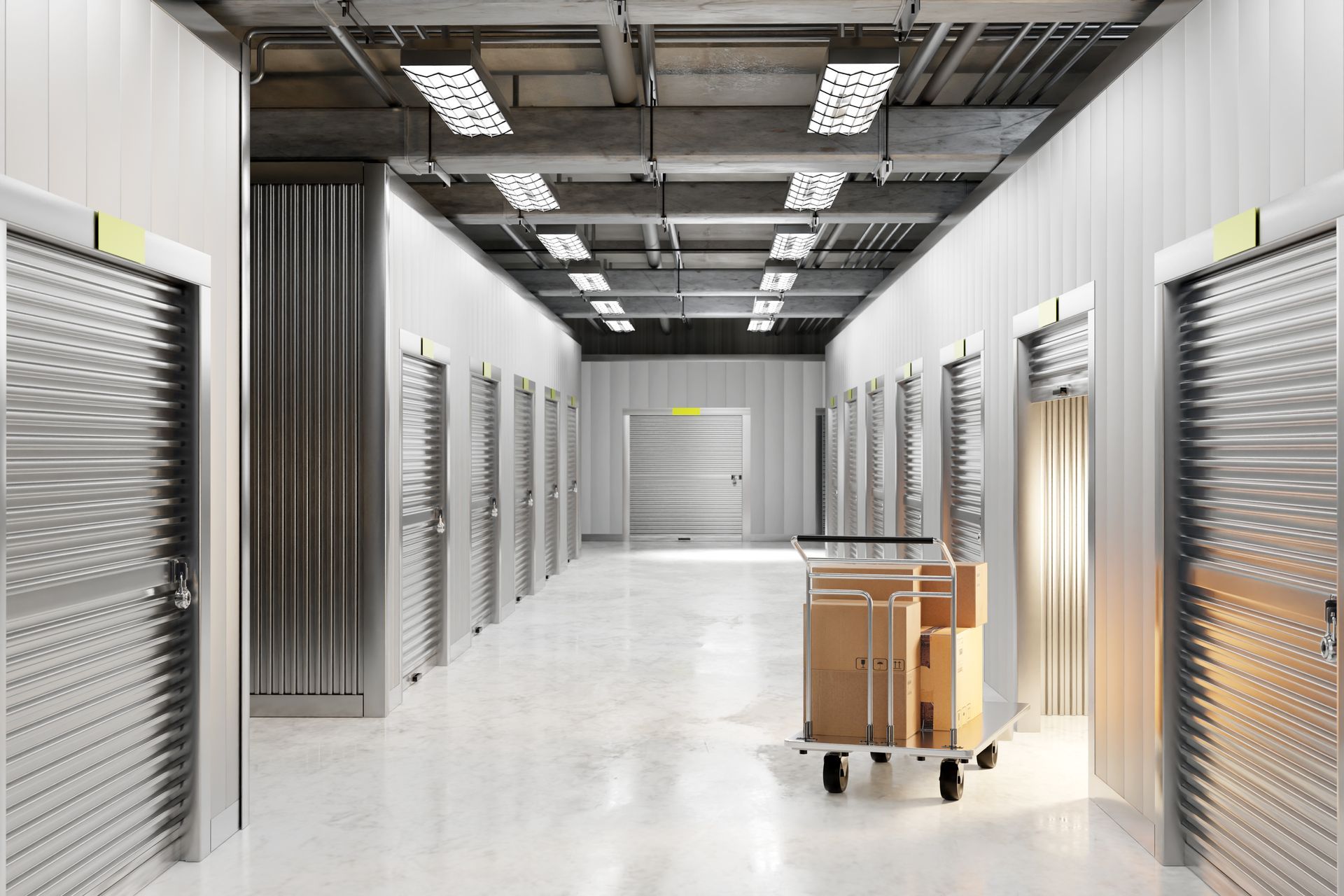 Clean self-storage facility hallway with multiple metal roll-up doors and a cart loaded with boxes.