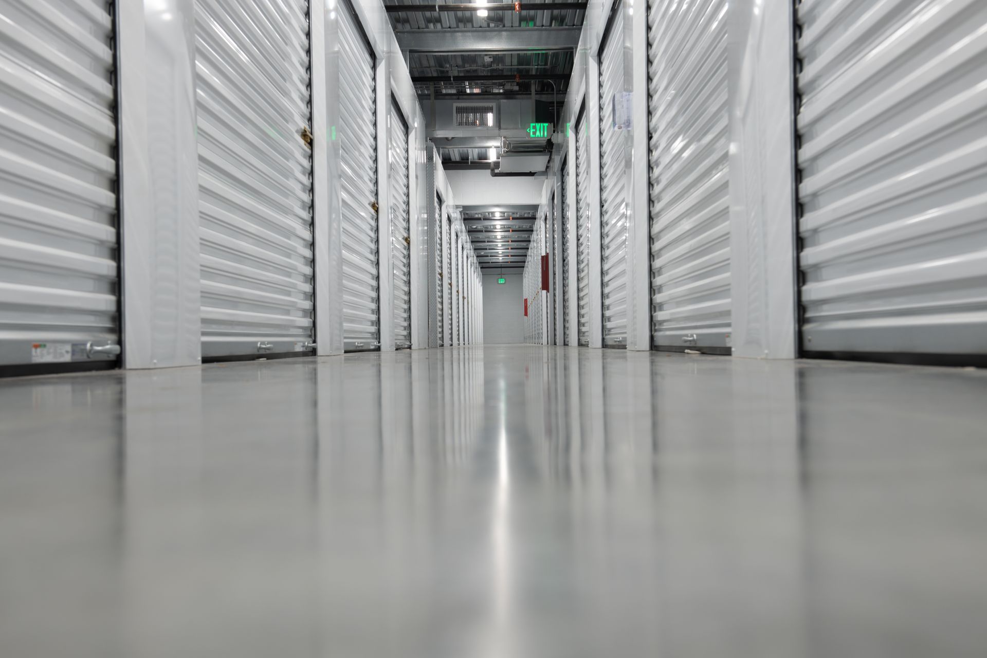Long hallway of storage units with closed metal doors and polished floor.