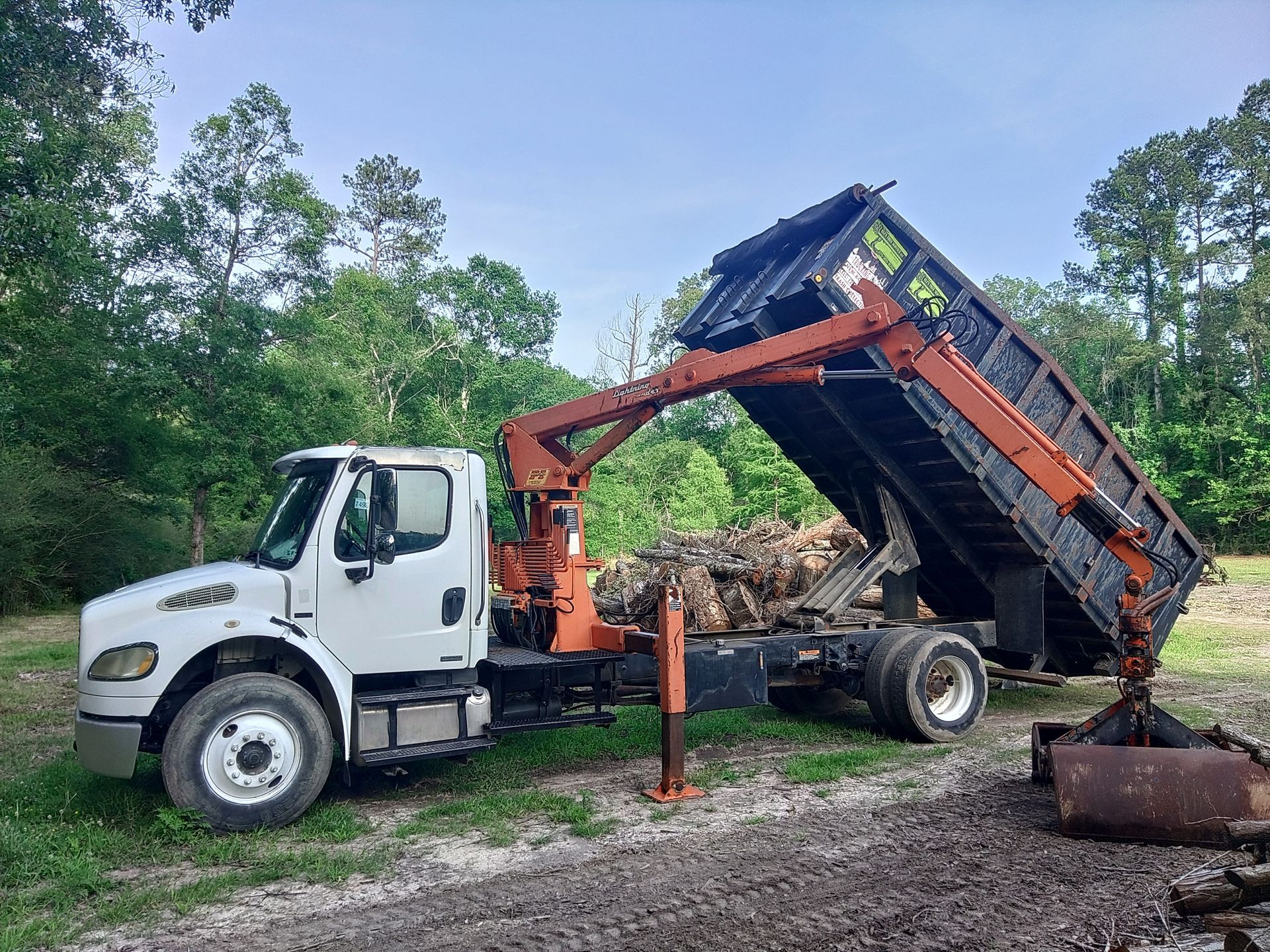 White dump truck raised to unload gravel in a wooded worksite