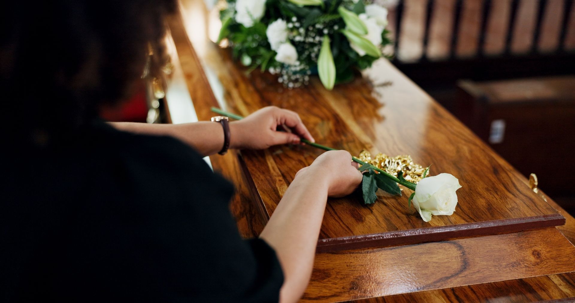 Man in glasses at a casket in a church, mourning. White flowers and somber setting.