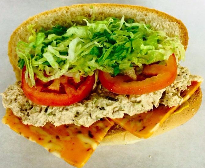 Open sandwich with lettuce, tomato slices, tuna salad, and a seeded bun on white background