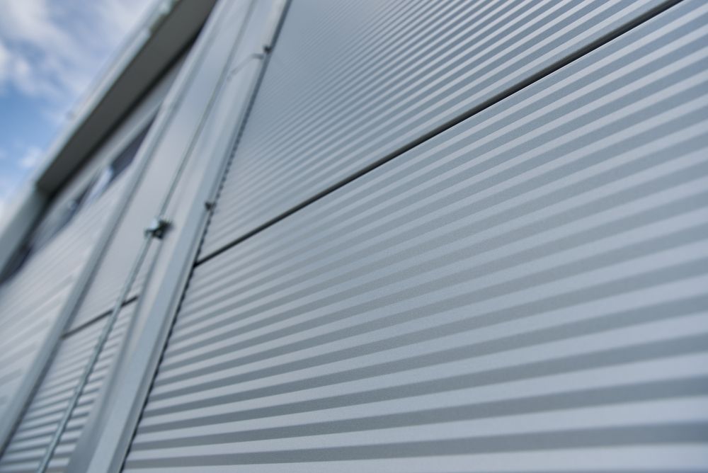 Close-up of a modern industrial building exterior with horizontal corrugated metal siding, a cloudy sky in the background.