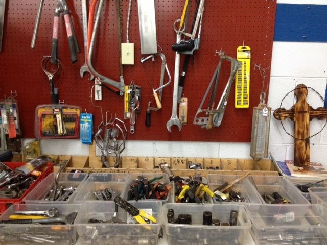 Workshop wall with hanging hand tools and bins of small parts on a red pegboard.