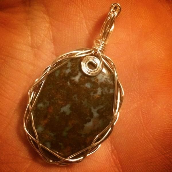 Oval silver wire-wrapped pendant with a dark mottled stone on a hand