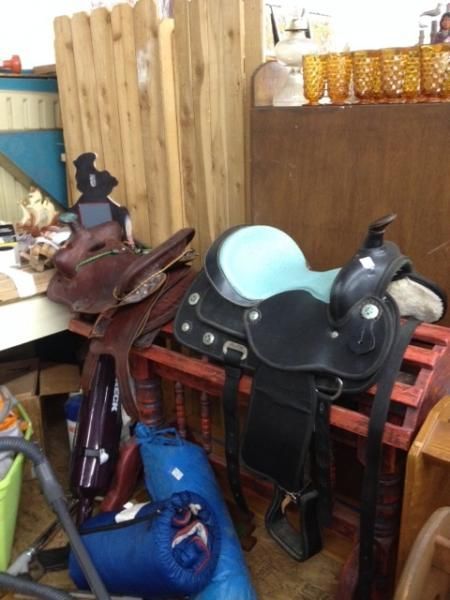 Stacked saddles and tack on a shelf in a rustic room