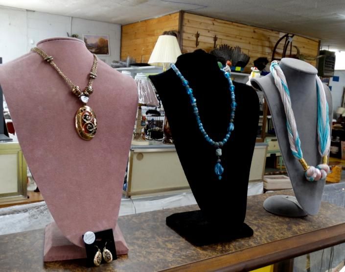 Three necklace display busts with jewelry in a store, in pink, black, and gray.