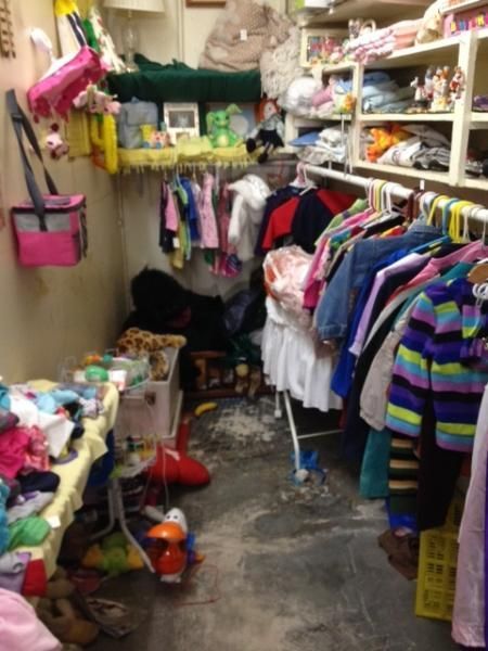 Cluttered thrift store aisle with colorful clothes hanging on racks and shelves of assorted items