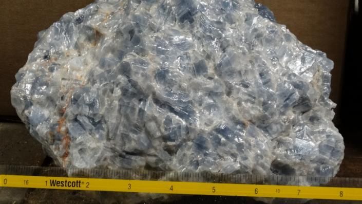 Large clear plastic bag filled with blue-gray scrap material on a ruler, against a dark background