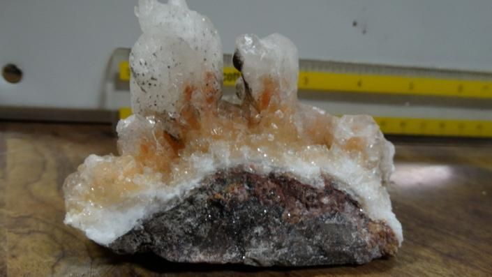 White and orange crystal mineral specimen on a dark rock base, photographed indoors on a table.