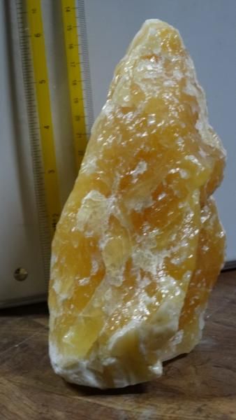 Large yellow-orange translucent crystal or rock specimen standing upright on a wooden surface