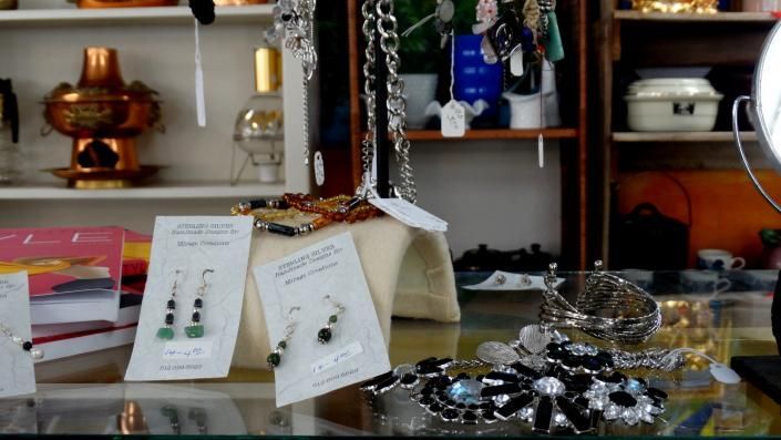 Jewelry display with necklaces, bracelets, and trays on a shop counter with shelves in the background