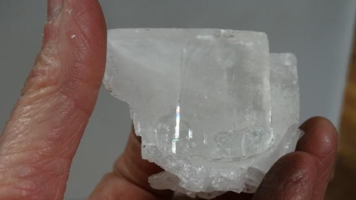 Hand holding a clear, translucent ice block with a rough, cloudy base