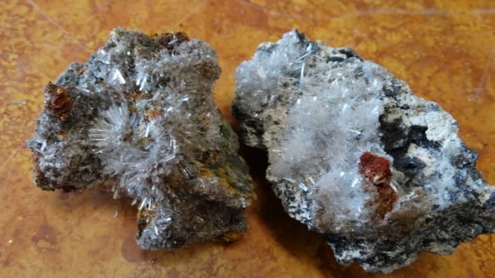 Two rough metallic rocks with silver-gray crystals and dark brown edges on a wooden surface