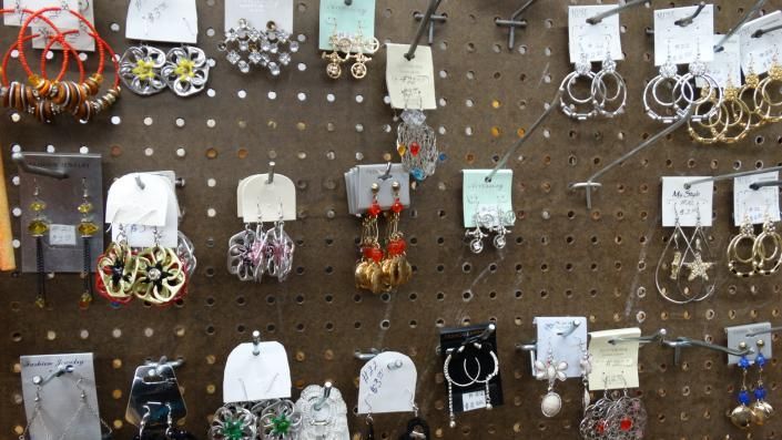 Display of assorted handmade earrings and jewelry hung on a brown pegboard.