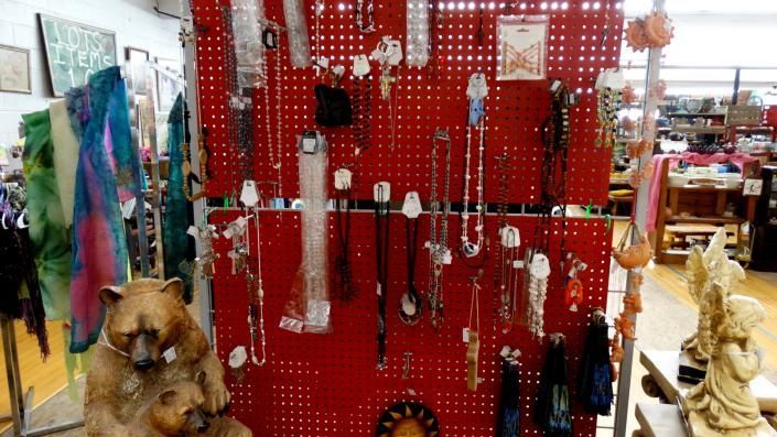 Red jewelry display with hanging necklaces and earrings in a shop, with a dog figurine at the lower left.