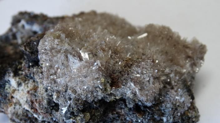 Close-up of a rough gray-brown rock with glittering crystals and dark mineral patches