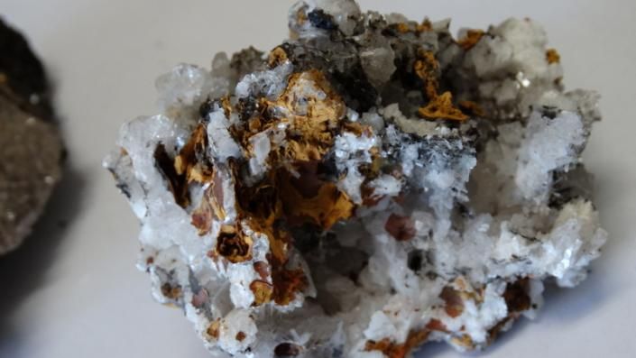 White and gray mineral rock with rusty brown-orange crystals on a light surface