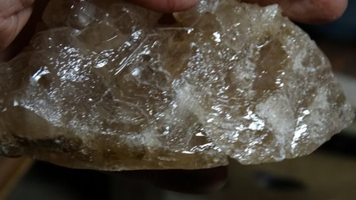 Close-up of a rough, translucent brownish crystal held in a hand against a dark background
