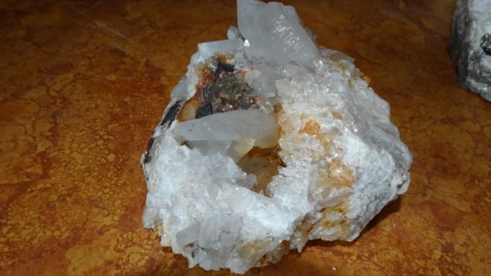 White translucent crystal cluster with a rough brownish rock base on a tabletop.