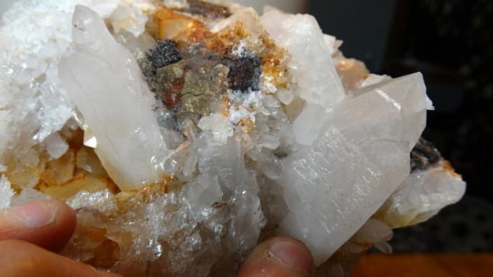 Hand holding a cluster of clear and white crystals with orange mineral staining