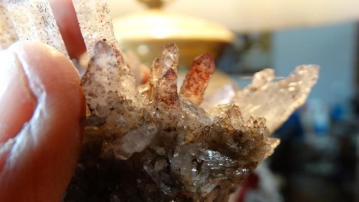 Close-up of a hand holding a small brown and clear crystal cluster against a blurred background