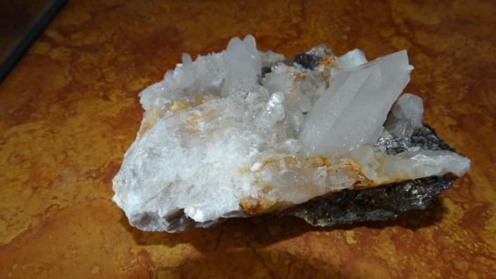 White crystal mineral cluster on a brown rock surface, with dark and orange mineral edges
