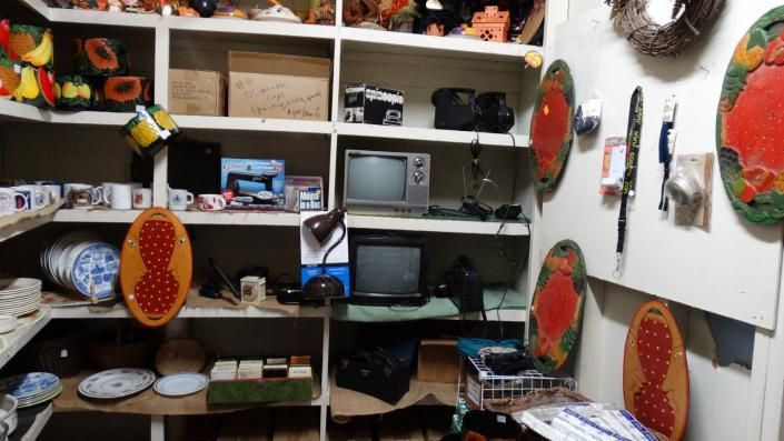 Cluttered craft room with shelves, a desk, TV, tools, and colorful round wall art.