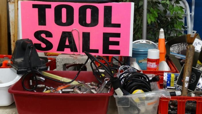 Tool sale sign behind bins of assorted used tools and hardware outdoors.