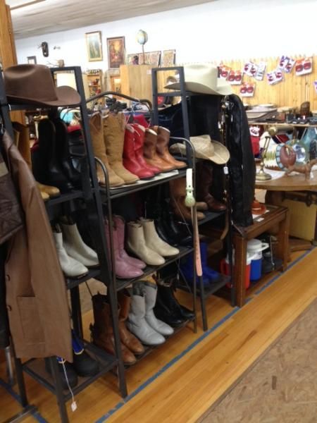 Boots and shoes displayed on black racks in a store aisle with a wooden floor.