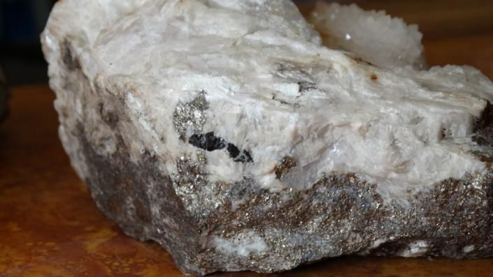 White and dark gray mineral rock with a rough, crystalline surface on a wooden table