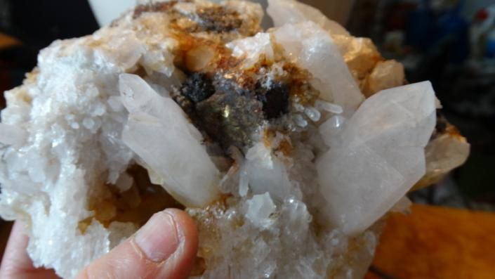 Hand holding a white quartz crystal cluster with brown and dark mineral inclusions