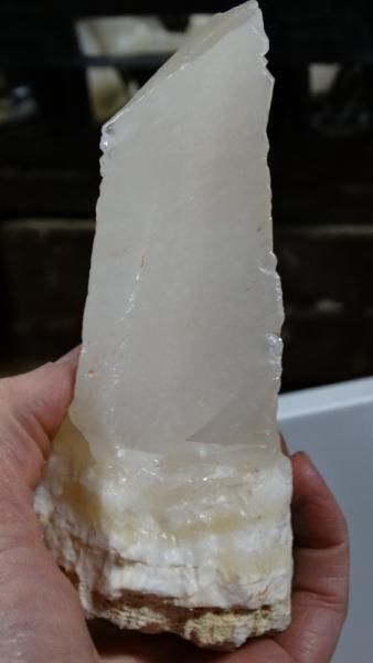 White translucent crystal on a beige mineral base, held upright in a hand.