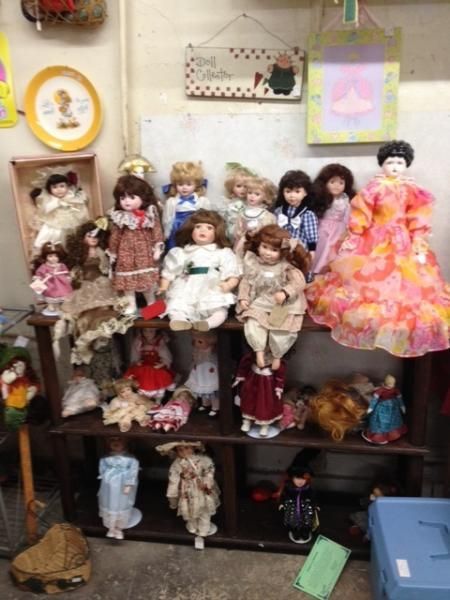 Shelf filled with assorted dolls and figurines, with one bright pink dress doll on the right