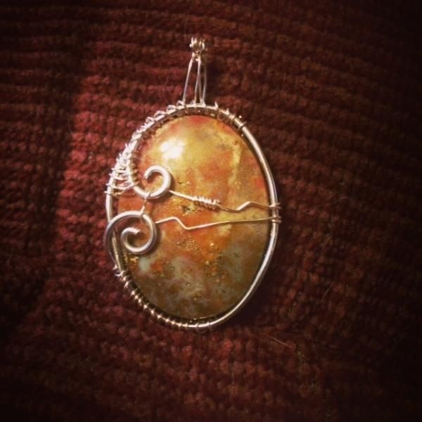 Oval amber pendant with silver wire swirls on a dark woven background