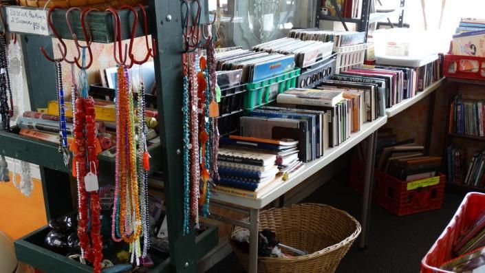 Display of colorful bracelets and books on shelves in a small shop, with baskets and hanging accessories.