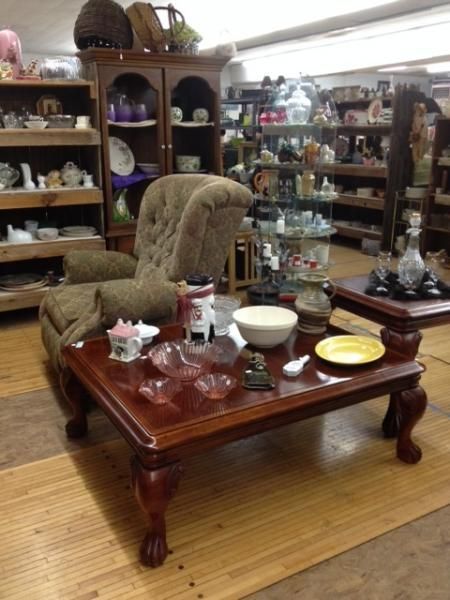 Antique furniture display with a wooden coffee table, upholstered chair, and shelves of decor in a shop