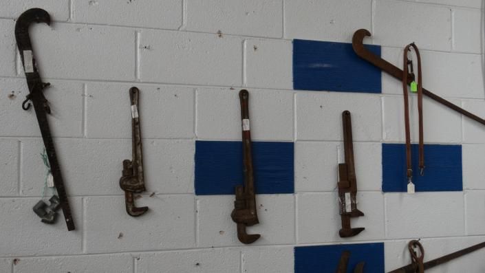 Assorted hand tools mounted on a white brick wall with blue square accents.