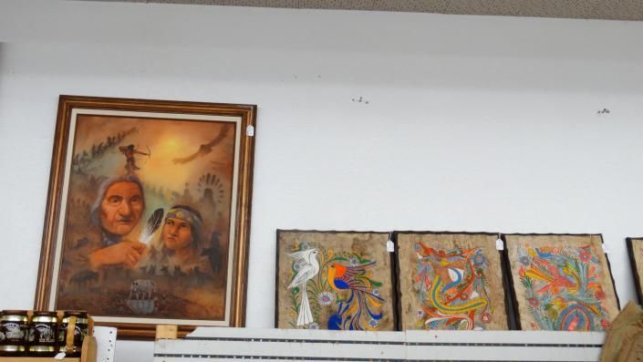 Framed portrait and three colorful abstract paintings leaning on a white shelf against a plain wall