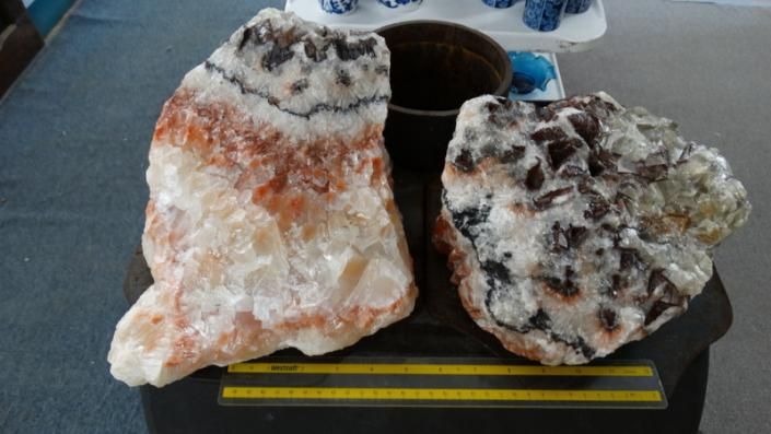 Two large mineral crystals on a black stand, one orange-white and one gray-white with dark streaks.