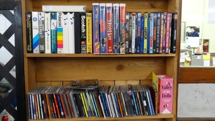 Wooden shelf filled with books and DVDs, with a pink bookend on the lower right.