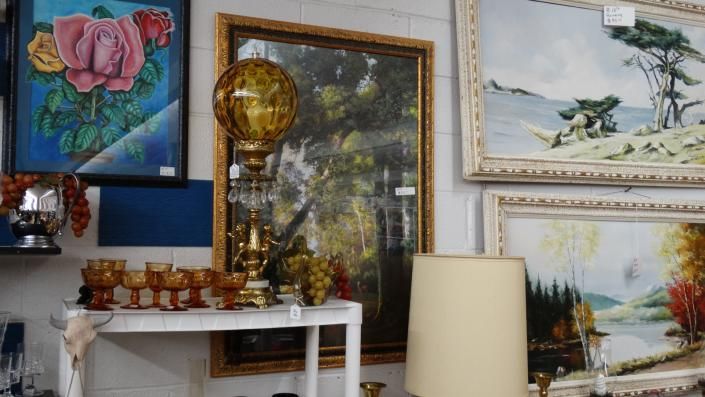 Art-filled room with framed paintings, a gold floor lamp, and a white mantel decorated with small figurines
