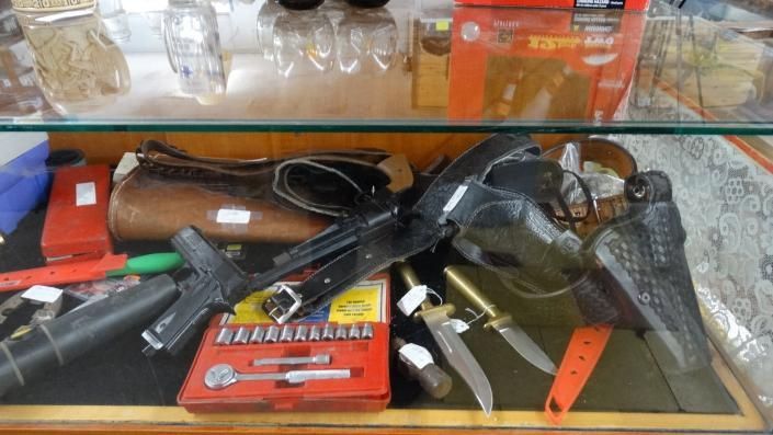 Assorted firearms and accessories displayed in a glass case with labels and packaging.
